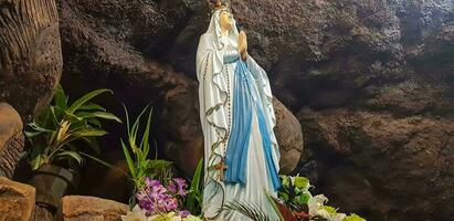 estatua de santo Virgen María en romano católico iglesia, en el cueva de Virgen María, en un rock cueva capilla católico Iglesia con tropical flores alrededor foto