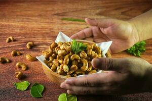 Cashew Nut, in Indonesia known as Kacang Mete or Mede, Served in a bowl on wood background, with hand photo