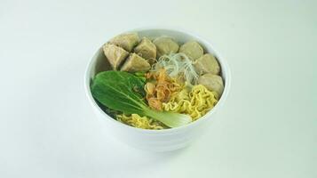 Meatball, in Indonesia known as Bakso or Baso. Served with noodles vegetables chili sauce in a bowl on white background with hand. Close up top view flat lay photo