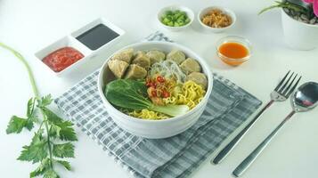 meatball, in Indonesia known as Bakso or Baso. Served with noodles vegetables chili sauce in a bowl on white background. Close up top view flat lay photo