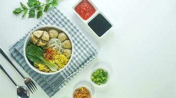 meatball, in Indonesia known as Bakso or Baso. Served with noodles vegetables chili sauce in a bowl on white background. Close up top view flat lay photo