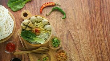 Meatball, in Indonesia known as Bakso or Baso. Served with noodles vegetables chili sauce in a bowl on wood background. Cclose up top view flat lay copy space photo