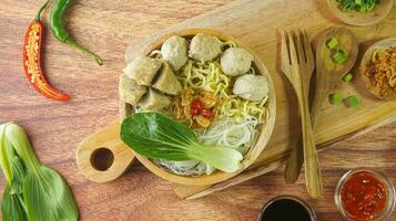 Meatball, in Indonesia known as Bakso or Baso. Served with noodles vegetables chili sauce in a bowl on wood background. Cclose up top view flat lay copy space photo