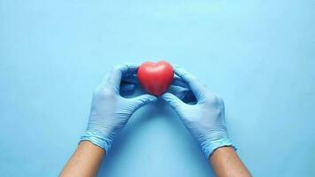 man hand in protective gloves holding red heart on blue video