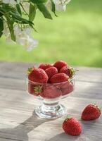 Ripe strawberries in a glass bowl on a wooden table in the garden. Summer still life with strawberries. Sunny day photo