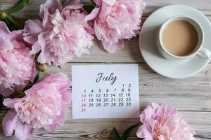July calendar, peonies and a cup of coffee on the table. Women's desktop photo