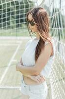 Beautiful stylish woman in summer dress standing on a football field near the grid photo