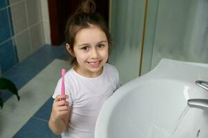Happy little Caucasian child girl, holding toothbrush, cleaning mouth. Healthy wellness development and fresh breath photo