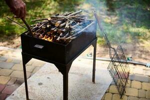 de cerca árbol ramas con un flameante fuego a comienzo un fuego en un parilla parrilla. picnic. comida al aire libre barbacoa parrilla fiesta foto