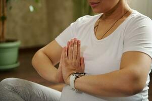Closeup gorgeous adult pregnant woman meditating at home, sitting in lotus position with clasped hands, practicing yoga photo