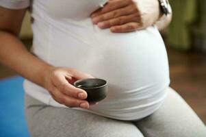 Closeup pregnant woman touching her belly while enjoying tea ceremony in chinese traditions after prenatal yoga practice photo