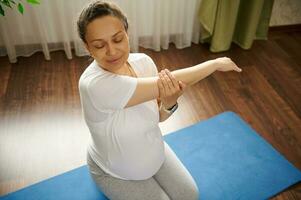 View from above of dult pregnant woman stretching her arms, sitting in hero pose on a blue exercise mat. Pregnancy yoga. photo