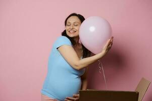 Delightful conscious pregnant woman gently hugging pink balloon, feeling happy positive emotions expecting a baby girl, photo