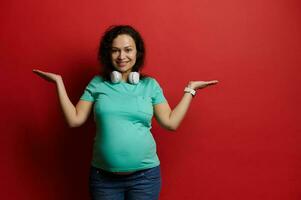 Beautiful pregnant woman, standing straight to camera, holds imaginary copy space on her hands palms up, isolated on red photo