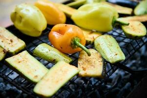 Selective focus on grilled bell pepper and sliced zucchinis over charcoal in the barbecue grill. Close-up. Picnic. photo