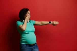 Beautiful frustrated pregnant woman checks contractions on mobile application on her wrist watch isolated red background photo