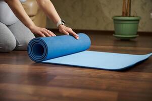 de cerca manos o embarazada mujer laminación fuera un estera mientras practicando yoga, prenatal extensión, respiración ejercicios interior foto