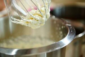 el proceso de flagelación crema a firma picos o huevo ropa blanca en planetario mezclador. azotado crema para pasteles y dulce postres foto