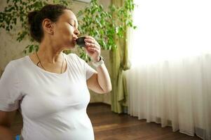 Multi ethnic beautiful pregnant woman drinking tea puer with healing antioxidants features after yoga practice at home photo