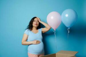 Pretty pregnant woman surprised by a gender reveal party, in anticipation of twins, expressing surprise on blue backdrop photo