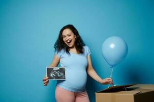 contento alegre embarazada mujer sonriente a cámara, participación ultrasonido escanear imagen de su recién nacido bebé chico. género fiesta foto