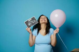 lleno de alegría embarazada mujer expresando positivo emociones esperando bebé chica, posando con rosado globo y ultrasonido escanear foto