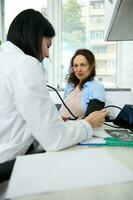 Happy pregnant woman at appointment with female doctor, obstetrician gynecologist. GP taking blood pressure in office photo