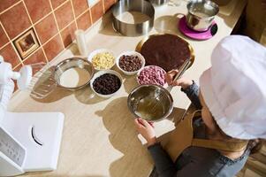 Overhead view of child girl confectioner using whisk, mixing ingredients in a metal bowl, standing by kitchen countertop photo