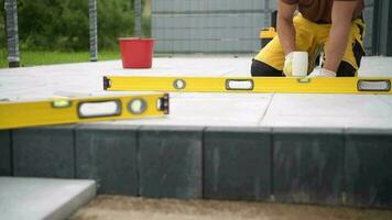 Kaukasisch bouw arbeider met professioneel hamer in zijn hand- gebouw beton tegels pad. bodem compactor machine in een achtergrond. video