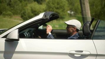 convertibile auto la libertà viaggio. caucasico autista nel il suo 30s indossare elegante berretto dietro a il ruota di moderno cabriolet veicolo. video