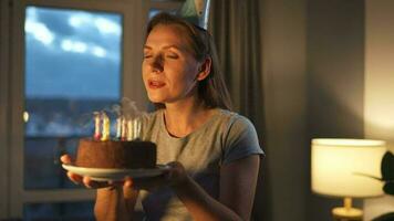 Happy excited woman making cherished wish and blowing candles on holiday cake, celebrating birthday at home, slow motion video