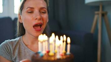 Happy excited woman making cherished wish and blowing candles on holiday cake, celebrating birthday at home, slow motion video