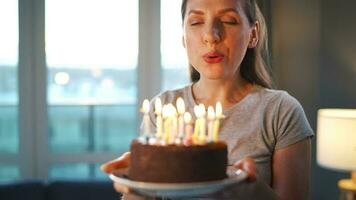 Happy excited woman making cherished wish and blowing candles on holiday cake, celebrating birthday at home, slow motion video