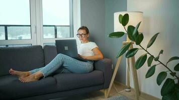 vrouw met bril is zittend Aan de bankstel en werken Aan een laptop. concept van afgelegen werk video