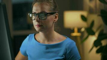 Woman in glasses looking on the monitor and surfing Internet at night. The monitor screen is reflected in the glasses. Work at night video