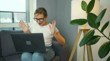 Casual dressed woman with glasses sitting on the sofa and communicates via video link with family or close friends