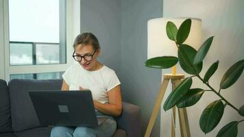 Casual dressed woman with glasses sitting on the sofa and communicates via video link with family or close friends