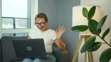 Casual dressed woman with glasses sitting on the sofa and communicates via video link with family or close friends