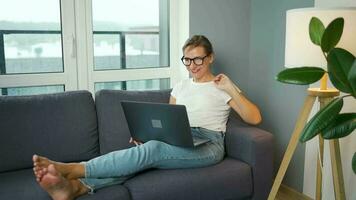 Casual dressed woman with glasses sitting on the sofa and communicates via video link with family or close friends