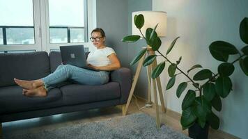 mujer con lentes es sentado en el sofá y trabajando en un ordenador portátil. concepto de remoto trabajo video