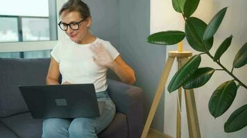 Casual dressed woman with glasses sitting on the sofa and communicates via video link with family or close friends