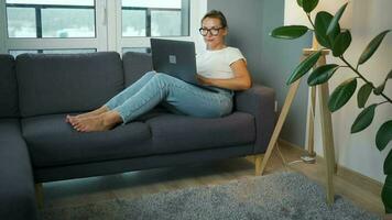 mujer con lentes es sentado en el sofá y trabajando en un ordenador portátil. concepto de remoto trabajo video