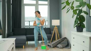 Woman in headphones cleans the house and have fun singing with a broom like a star at a concert video