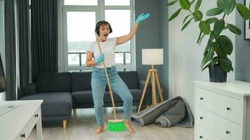 Woman in headphones cleans the house and have fun singing with a broom like a star at a concert video