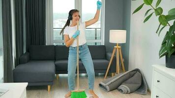 Woman in headphones cleans the house and have fun singing with a broom like a star at a concert video