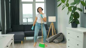 Woman in headphones cleans the house and have fun singing with a broom like a star at a concert video