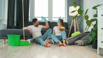 Tired couple sits on the floor in a room and high five each other after they finish cleaning the house video