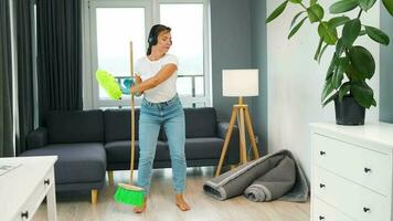 Woman in headphones cleaning the house and having fun dancing with a broom and washcloth. video