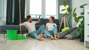 Tired couple sits on the floor in a room and high five each other after they finish cleaning the house video