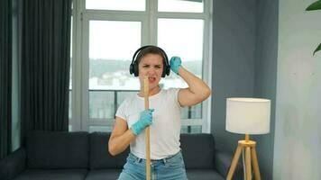 Woman in headphones cleans the house and have fun singing with a broom like a star at a concert video